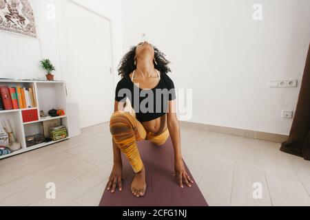Anonyme afro-américaine jeune femme attrayante assise dans le yoga pose avec les yeux fermés sur le tapis dans la pièce lumineuse Banque D'Images