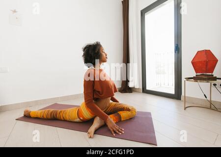 Afro-américaine jeune femme attrayante assise dans une posture de yoga avec les yeux fermés sur le tapis dans la pièce lumineuse Banque D'Images