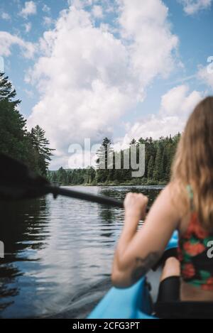 Vue arrière de la femme voyageur anonyme dans la vie gilet assis dans le bateau pendant l'exploration de la rivière contre le ciel nuageux dans le parc national de la Mauricie, au Québec, Canada Banque D'Images