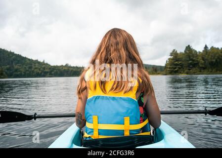 Vue arrière de la femme voyageur anonyme dans la vie gilet assis dans le bateau pendant l'exploration de la rivière contre le ciel nuageux dans le parc national de la Mauricie, au Québec, Canada Banque D'Images