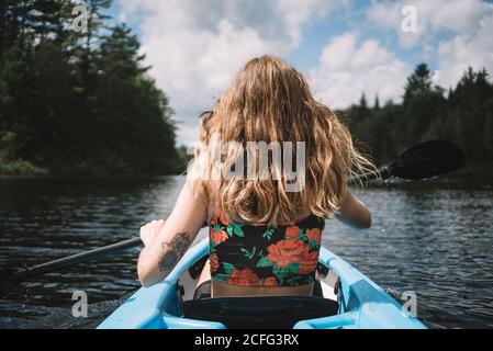 Vue arrière de la femme voyageur anonyme dans la vie gilet assis dans le bateau pendant l'exploration de la rivière contre le ciel nuageux dans le parc national de la Mauricie, au Québec, Canada Banque D'Images