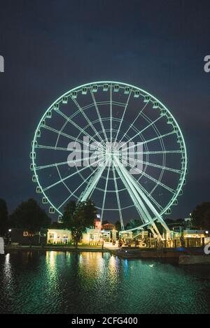 Grande roue lumineuse bleue dans le parc d'attractions sur la jetée de Ville de Montréal se reflétant dans l'eau de la rivière la nuit Banque D'Images