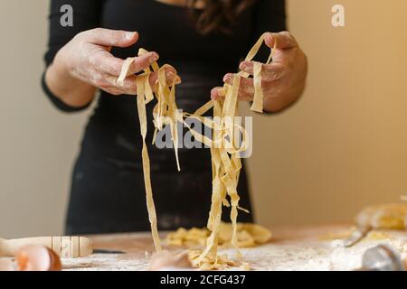 Femme tenant couper fines bandes de pâtes dans les mains pendant préparation du repas dans la cuisine Banque D'Images