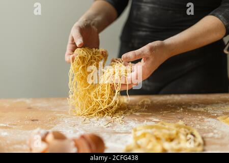 Femme tenant couper fines bandes de pâtes dans les mains pendant préparation du repas dans la cuisine Banque D'Images