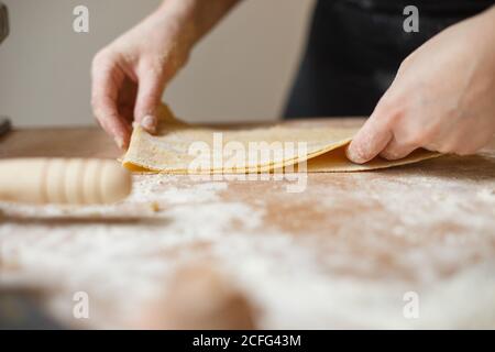 cuisson non reconnaissable en pâte à pâtes fine roulée, pliante et noire dans plusieurs couches pendant la préparation de la pâtisserie sur la table avec farine Banque D'Images