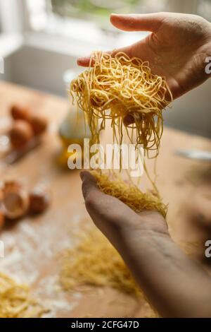 Femme tenant couper fines bandes de pâtes dans les mains pendant préparation du repas dans la cuisine Banque D'Images