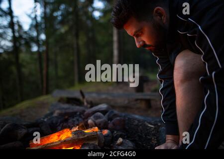 Vue latérale d'un homme tranquille assis près d'un feu de camp dans les bois et réchauffez-vous tout en profitant du week-end Banque D'Images