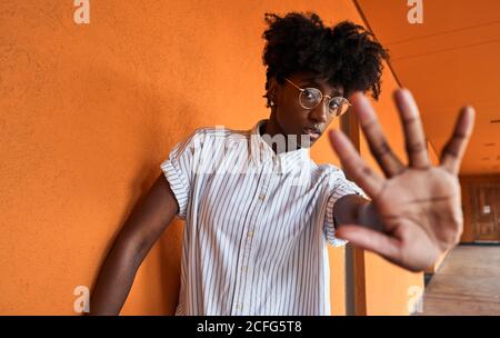 Femme afro-américaine adulte avec les yeux fermés essayant d'arrêter impact négatif en se tenant debout avec les bras relevés contre flou vif intérieur orange dans le couloir du bâtiment moderne Banque D'Images