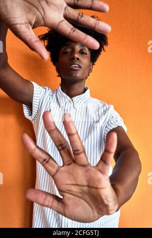 Femme afro-américaine adulte avec les yeux fermés essayant d'arrêter impact négatif en se tenant debout avec les bras relevés contre flou vif intérieur orange dans le couloir du bâtiment moderne Banque D'Images