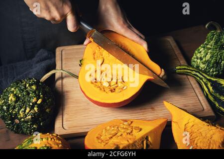 récolte d'automne - femme coupant de la citrouille pour cuisiner sur du bois carte Banque D'Images