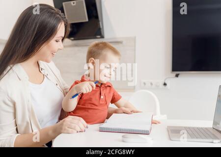 Belle femme aide son fils à apprendre à écrire des lettres d'alphabet. Concept d'apprentissage en ligne Banque D'Images