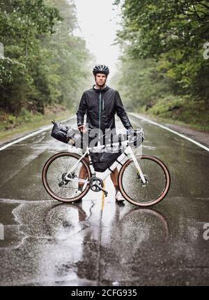 Un emballeur de vélo mâle se tient avec le vélo dans la route dans la pluie battante, Maine Banque D'Images