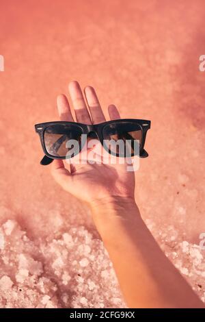 Femme tenant des lunettes de soleil au-dessus de l'eau rose Banque D'Images