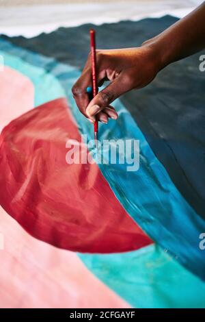 De haut en haut de crop anonyme noir femelle avec dessin de pinceau image colorée sur papier assis sur le sol à la maison Banque D'Images