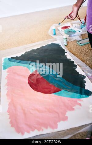 De haut en haut de crop anonyme noir femelle avec dessin de pinceau image colorée sur papier assis sur le sol à la maison Banque D'Images
