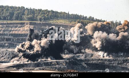 Des engins explosifs sont à ciel ouvert dans l'industrie des mines de charbon. Poussière et bouffées de fumée dans le ciel, sol sablé Banque D'Images