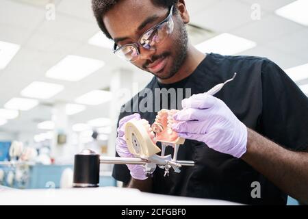 Afro-américain gars en latex gants utilisant le miroir de bouche et sonde permettant de vérifier les fausses dents lors de travaux dans un laboratoire moderne Banque D'Images