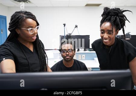 Les femmes noires et l'homme en uniforme discutant des données sur l'ordinateur tout en travaillant ensemble dans un laboratoire contemporain Banque D'Images