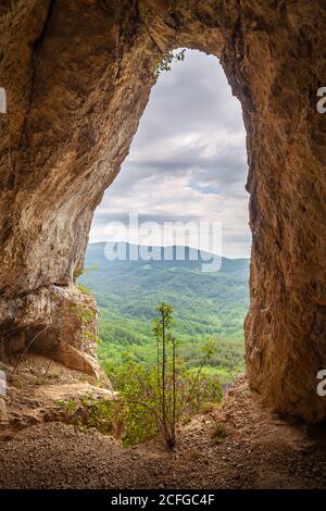 Vue incroyable à travers le trou dans le rocher avec rouge rochers sur les murs autour sur les montagnes lointaines et forêts au début du printemps Banque D'Images