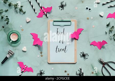 Arrière-plan Halloween sur fond vert menthe. Plat avec brindilles d'eucalyptus, chauves-souris en papier rose vif, confetti, coeurs de sucre, bruiteurs de fête, dri Banque D'Images