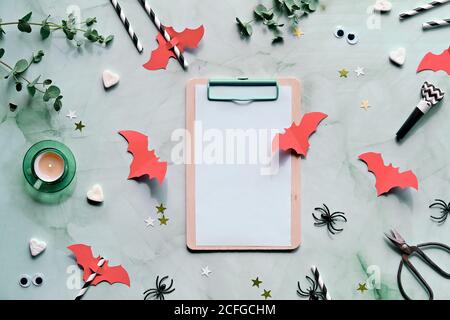 Arrière-plan Halloween sur fond vert menthe. Plat avec brindilles d'eucalyptus, chauves-souris en papier rouge corail, confetti, coeurs de sucre, bruiteurs de fête, boisson Banque D'Images