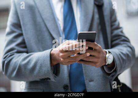 photo sans visage d'homme d'affaires noir en costume et montre avec un smartphone à l'extérieur. Banque D'Images