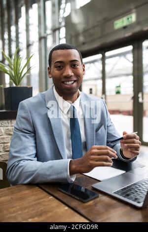 Jeune homme afro-américain en costume bleu assis à une table en bois Banque D'Images