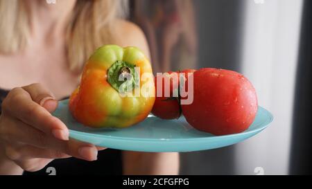 Tomate et poivre sur une assiette bleue sur un fond clair sur la cuisine. Femme tenant une assiette avec des légumes frais. Banque D'Images