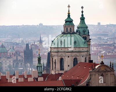 Prague depuis le château : une vue d'ensemble brumeuse tôt le matin de la ville et de ses clochers depuis le parc du château. Le dôme de Saint-Nicolas domine le passé avec le pont Charles au milieu du sol. Banque D'Images