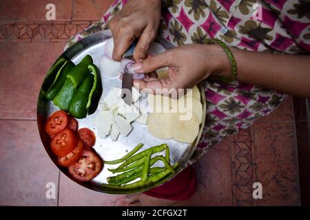 Femme indienne hacher des oignons à l'aide d'un couteau avec les deux mains sur Thali. Préparation pour préparer le Pakoda ou le curry sabji sur thali. Méthode traditionnelle o Banque D'Images