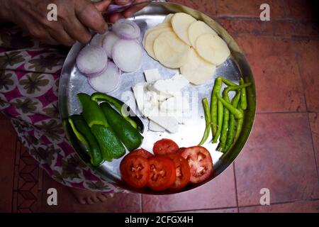 Femme indienne hacher des oignons à l'aide d'un couteau avec les deux mains sur Thali. Préparation pour préparer le Pakoda ou le curry sabji sur thali. Méthode traditionnelle o Banque D'Images