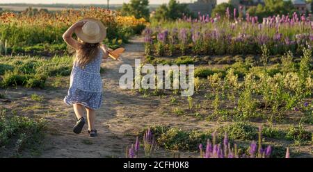 enfance, provence style concept - bannière 3 ans blonde petite fille enfant en robe bleue et chapeau de paille aspect slave courir le long du chemin avec le jouet Banque D'Images