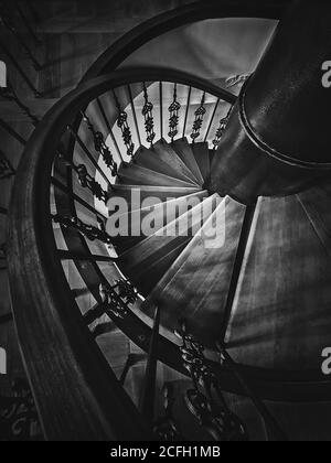 Vue sur un vieux escalier en colimaçon. Escalier circulaire en bois avec balustrade métallique ornée, plan vertical noir et blanc, architecture intérieure de Banque D'Images