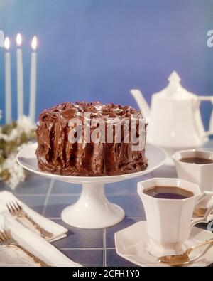GÂTEAU GLACÉ AU CHOCOLAT DES ANNÉES 1970 SUR SUPPORT À GÂTEAU BLANC CAFETIÈRE TASSES ET SOUCOUPES FOURCHETTES SERVIETTES TROIS BOUGIES BLEUES - KF8548 PHT001 DOSSIER DE TABLE HARS Banque D'Images
