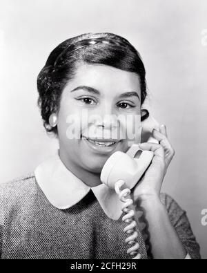 DANS LES ANNÉES 1950, UNE FEMME AFRO-AMÉRICAINE SOURIANTE PARLE AU TÉLÉPHONE APPAREIL PHOTO - N157 HAR001 HARS PERSONNES EXPRESSIONS B&W CONTACT VISUEL LE BONHEUR EST À LA TÊTE ET AUX ÉPAULES DE L'ETHNIE NOIRE AFRO-AMÉRICAINE SUR LES PROFESSIONS TÉLÉPHONES CONNEXION TÉLÉPHONES RELAXATION JEUNE ADULTE FEMME NOIR ET BLANC HAR001 AFRO-AMÉRICAINS À L'ANCIENNE Banque D'Images