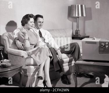 ANNÉES 1950 COUPLE CONTENT HOMME FEMME MARI FEMME ASSIS SUR UN CANAPÉ DANS LE SALON FUMEUR REGARDANT LA TÉLÉVISION PORTABLE - R518 HAR001 HARS COUCH COMMUNICATION PAIX ÉQUILIBRE INFORMATION HEUREUX JOIE STYLE DE VIE SATISFACTION FEMMES MARIÉE CONJOINT ÉPOUX VIE À LA MAISON COPIE ESPACE PLEINE LONGUEUR FEMMES PERSONNES HOMMES DIVERTISSEMENT PORTABLE B&W PARTENAIRE GRAND ANGLE RÊVES BONHEUR GAI PROTECTION RÉSEAU CHOIX EXCITATION DIVERTISSEMENT SUR LES SOURIRES CONNEXION ENGROSED CONCEPTUEL JOYFUL ÉLÉGANT CONTENTED MI-ADULTE MOYEN-ADULTE HOMME MOYEN-ADULTE FEMME RELAXATION TOGETHERNESS FEMMES ABSORBAIENT NOIR ET BLANC Banque D'Images