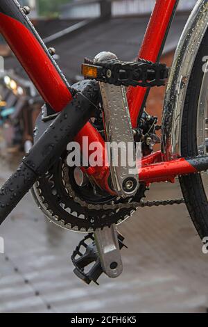 Vue en gros plan des pédales de vélo humides et du disque de frein avec la plaquette de frein de la roue arrière sur fond urbain Banque D'Images