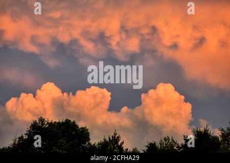 Ciel spectaculaire avec des cumulus de nuages de billonnement teinté de teintes brillantes d'orange et de rose juste avant le coucher du soleil. Banque D'Images