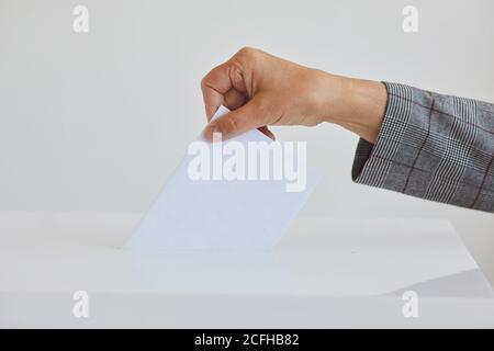 Vue latérale gros plan de la main féminine mettant le bulletin de vote dans l'urne sur fond blanc le jour de l'élection, espace de copie Banque D'Images