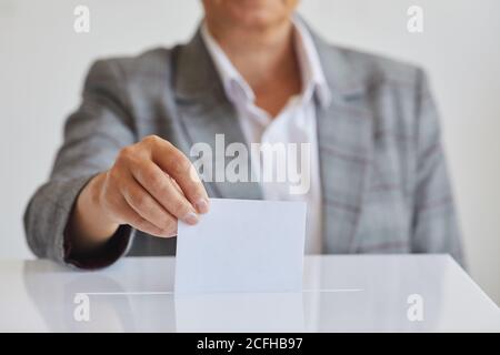 Vue de face gros plan de la main féminine mettant le bulletin de vote dans l'urne sur fond blanc le jour de l'élection, espace de copie Banque D'Images