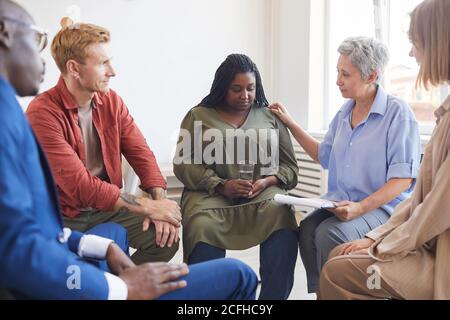 Portrait de la jeune femme afro-américaine partageant des luttes pendant le groupe de soutien rencontre avec des gens qui la trouvent en cercle et la réconfortant Banque D'Images