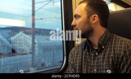 Un homme sérieux et confiant regarde par la fenêtre d'un train. Banque D'Images