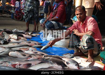 Négociant asiatique de poissons attendant des clients à son magasin dans Un marché local de poissons du Bangladesh rural Banque D'Images