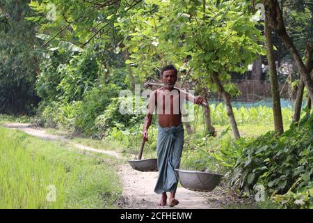 Agriculteur asiatique transportant des outils agricoles (bêche, bols) pour travailler dans les terres agricoles les plus proches de la campagne de Bogura, au Bangladesh Banque D'Images