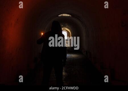L'homme dans le capot avec une bougie dans sa main a trouvé un moyen de sortir du passage souterrain sombre et va à la porte éclairée à l'extrémité du tunnel. Banque D'Images