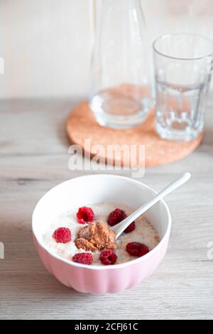 Lait de flocons d'avoine avec baies de framboises fraîches dans un bol blanc sur la table. Petit-déjeuner en-cas l'après-midi. Photo verticale Banque D'Images