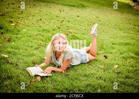 Jeune femme couché sur l'herbe lisant un livre, regardant loin Banque D'Images