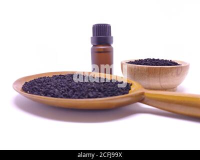 Bouteille en verre d'huile essentielle de graines de cumin noir , Nigella Sativa dans une cuillère en bois et un bol sur fond blanc. Concept de médecine à base de plantes Banque D'Images