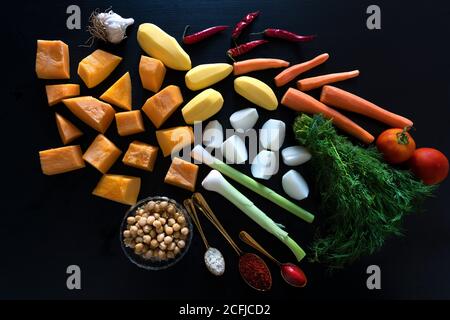 Nourriture sur une table. Photo de haute qualité. Légumes hachés sur fond noir. Citrouille, pommes de terre, ail, piments, carottes, tomates, oignons. Une cuillère à café d'or avec pâte de tomate, une cuillère à café d'or avec sel de l'Atlantique, une cuillère à café d'or avec paprika, aneth, coagulation, un bol de pois chiches. Ingrédients pour préparer du couscous. Banque D'Images