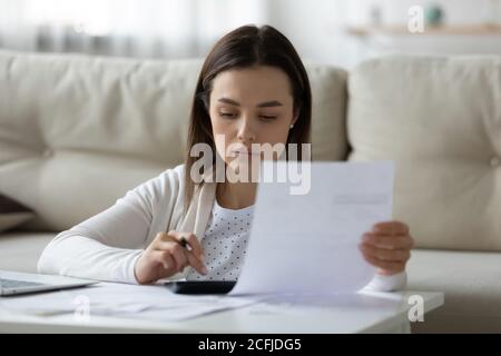 Femme sérieuse calculant le budget du ménage seule à la maison. Banque D'Images